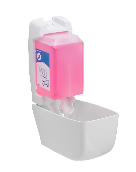 Weißer, wandmontierter Seifenspender mit durchsichtiger, rechteckiger pinkfarbener Seifenkartusche oben. Am Auslauf ist bereits pinkfarbener Schaum sichtbar, bereit zur Abgabe. Blau-weißes Etikett „Scott“.