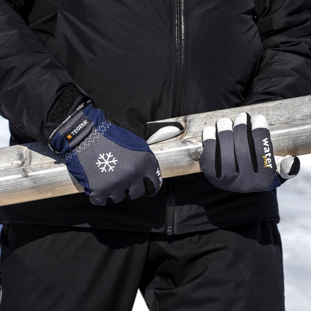 Person in schwarzer Winterjacke hält Holzplanke. Trägt blaue, graue und weiße Kälteschutzhandschuhe TEGERA 295. Links weiße Schneeflocke, rechts Schriftzug „waterproof“. Ideal für Arbeit in Kälte und Nässe.
