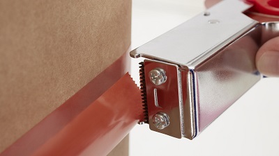 Oranges tesa Strapping-Klebeband wird mit silbernem Abroller von Hand um ein braunes, zylindrisches Objekt gewickelt oder abgetrennt. Der Abroller hat ein gezacktes Messer zum Schneiden des reissfesten Bands.