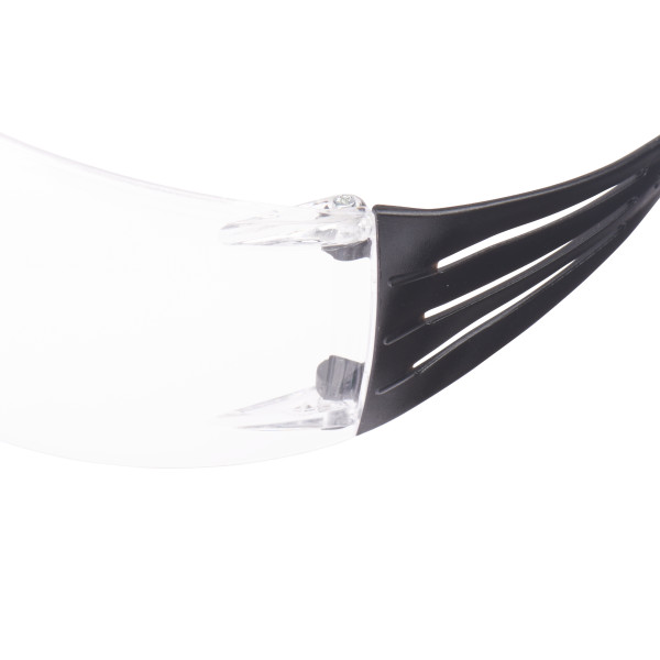Nahaufnahme einer 3M SecureFit Schutzbrille mit transparentem Polycarbonatglas und schwarzem Bügel. Das Glas hat Antikratz- und Antibeschlagbeschichtung. Der Bügel besitzt flexible, gerippte Details für gleichmäßige Druckverteilung.