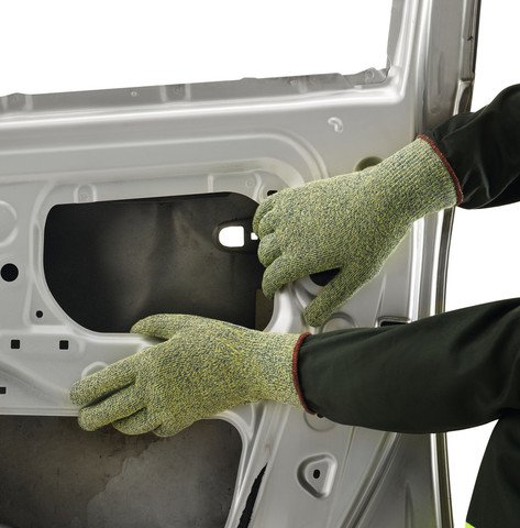 Zwei Hände in grüngelben Schnittschutzhandschuhen mit roten Bündchen arbeiten präzise an der Innenstruktur einer silbernen Autotür. Die robusten Handschuhe schützen bei Montage und bieten sicheren Halt beim Umgang mit scharfkantigen Metallteilen.