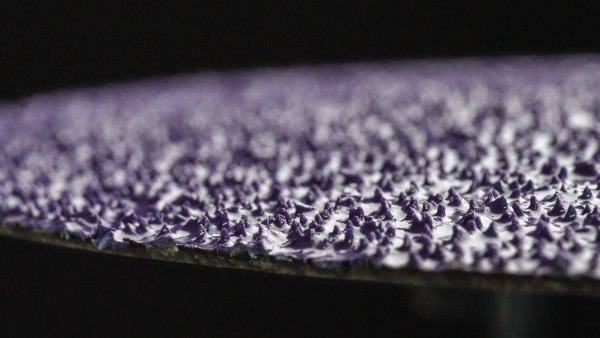 Gros plan sur une surface abrasive violet foncé, parsemée de grains de précision pointus et densément disposés. La texture irrégulière et rugueuse du disque en fibre Cubitron 3 est clairement visible et souligne son excellent pouvoir abrasif.