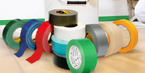 Mehrere Rollen Klebeband in leuchtenden Farben liegen auf hellem Boden vor einem weißen Eimer. Zu sehen sind grüne, blaue, rote, weiße, graue, beige und orange Bänder, darunter Maler- und Gewebeband für Renovierung.